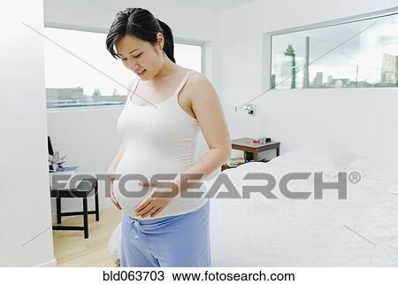 Stock Image - Pregnant Asian woman holding stomach. Fotosearch