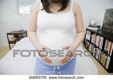 Stock Photography - Pregnant Asian woman holding stomach. Fotosearch