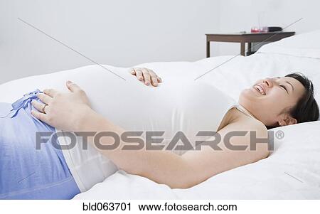 Stock Image - Pregnant Asian woman laying on bed. Fotosearch