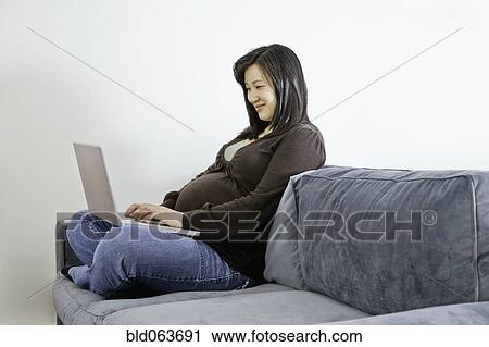 Pregnant Asian woman on sofa with laptop View Large Photo Image Stock Image - Pregnant Asian woman on sofa with laptop. Fotosearch