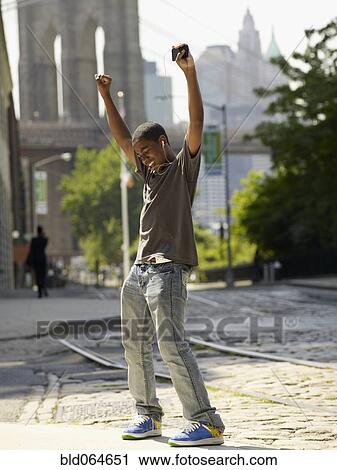 Stock Image - African boy listening to mp3 player in urban setting. Fotosearch