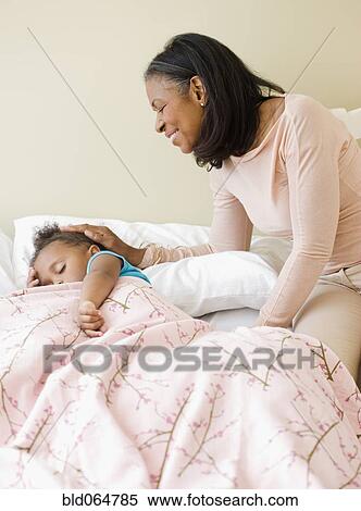 Stock Photography - African grandmother checking on sleeping granddaughter. Fotosearch