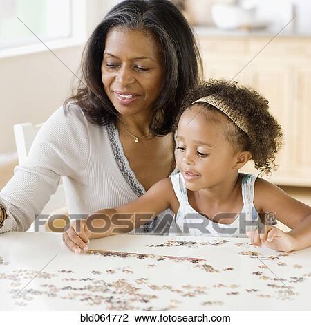 Stock Image - African grandmother helping granddaughter put together a puzzle. Fotosearch