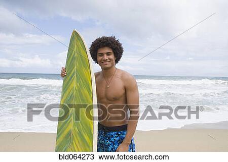 Stock Image - African man at beach with surfboard. Fotosearch