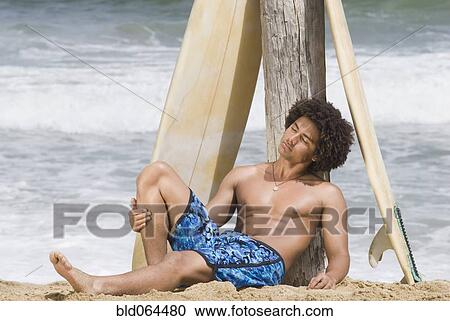 Stock Image - African man at beach with surfboard. Fotosearch