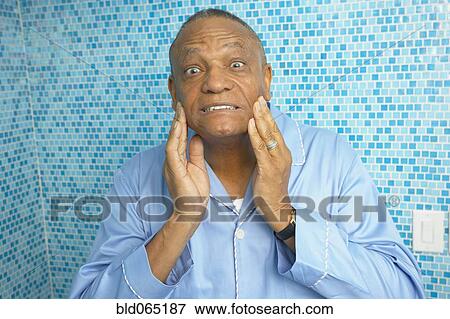 Stock Photo - African man checking is wrinkles in bathroom. Fotosearch