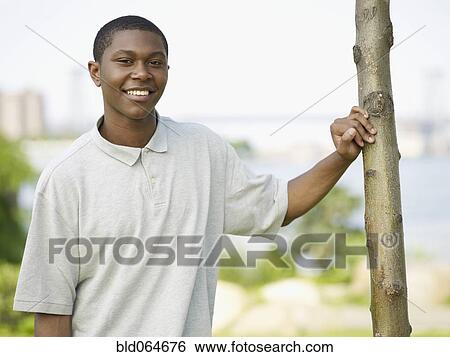 Stock Photograph - African man leaning on tree trunk in park. Fotosearch