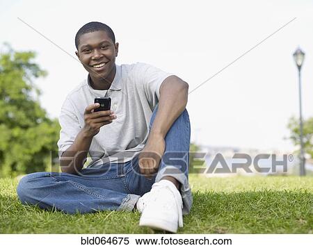 African man sitting in park text messaging on cell phone View Large Photo Image Stock Photography - African man sitting in park text messaging on cell phone. Fotosearch
