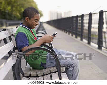 Stock Image - African teenager text messaging on cell phone. Fotosearch