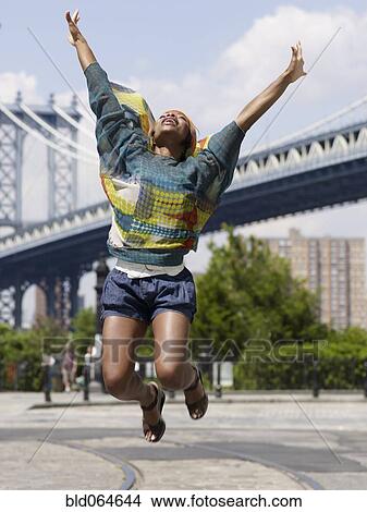 Picture - African woman jumping in mid-air in urban setting. Fotosearch