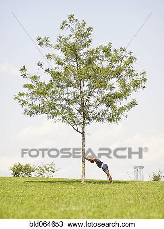 Stock Image - African woman leaning against tree in park. Fotosearch