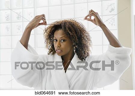 Stock Image - African woman pulling frizzy hair in bathroom. Fotosearch