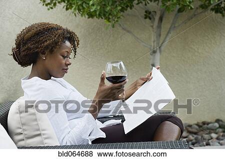 Stock Photo - African woman reading on patio and drinking red wine. Fotosearch