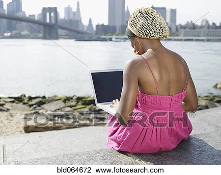 African woman sitting at urban waterfront typing on laptop View Large Photo Image Stock Image - African woman sitting at urban waterfront typing on laptop. Fotosearch