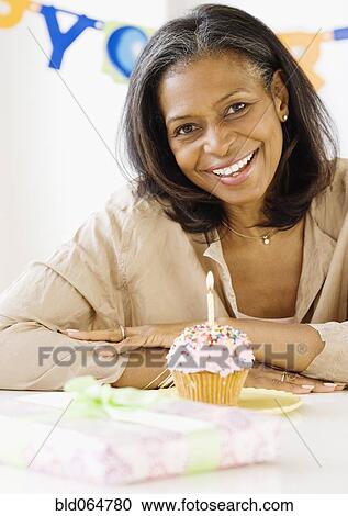 Stock Image - African woman smiling with birthday candle in cupcake. Fotosearch