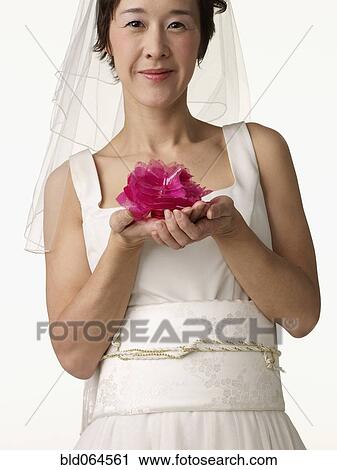 Stock Image - Asian woman in wedding dress holding flower. Fotosearch