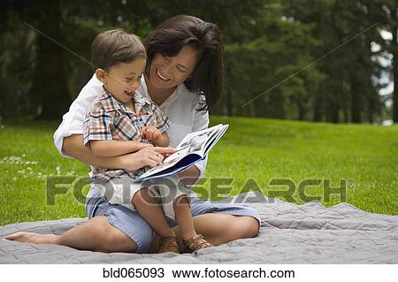 Stock Image - Boy reading story book in park with mother. Fotosearch