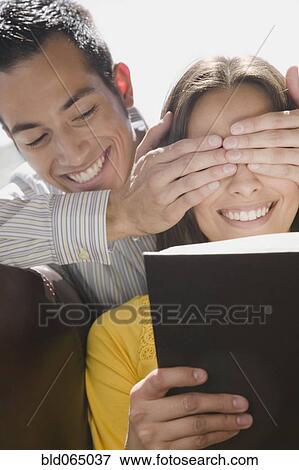 Stock Photo - Boyfriend covering girlfriend’s eyes. Fotosearch