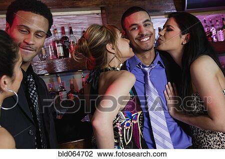 Stock Image - Businessman being kissed by two women in bar. Fotosearch