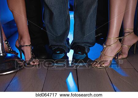Stock Photo - Close up of women’s glamorous feet and man’s sneakers. Fotosearch