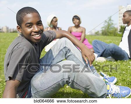 Stock Photograph - Confident African boy sitting in park with friends. Fotosearch