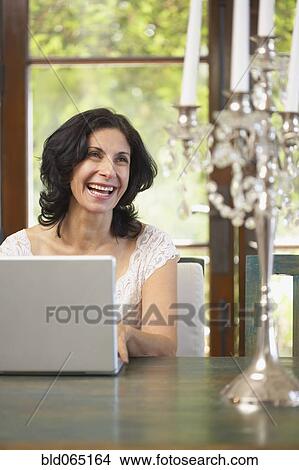 Picture - Confident Middle Eastern woman typing on laptop in dining room. Fotosearch
