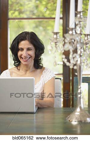 Confident Middle Eastern woman typing on laptop in dining room View Large Photo Image Stock Image - Confident Middle Eastern woman typing on laptop in dining room. Fotosearch