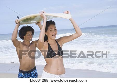 Stock Photo - Couple carrying surfboard at beach. Fotosearch