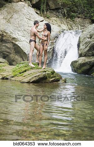Stock Image - Couple standing in pool near waterfall. Fotosearch