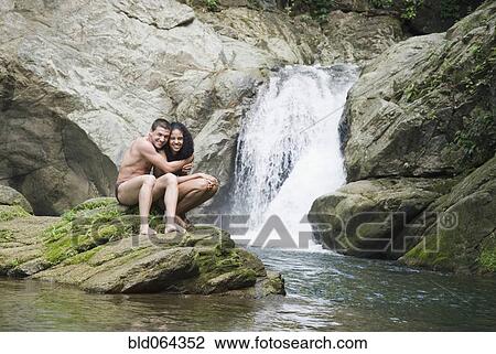 Stock Image - Couple swimming in pool near waterfall. Fotosearch