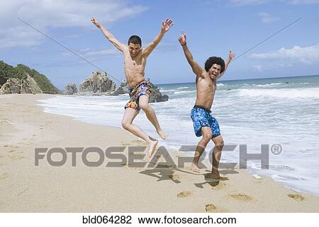 Stock Image - Friends at beach jumping in mid-air. Fotosearch