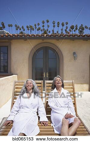 Stock Image - Friends laying on lounge chairs at resort. Fotosearch