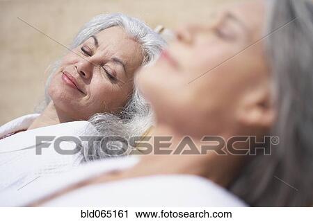 Stock Image - Friends sleeping on lounge chairs at resort. Fotosearch