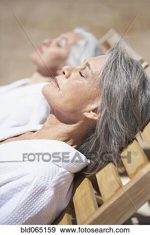 Stock Photo - Friends sleeping on lounge chairs at resort. Fotosearch