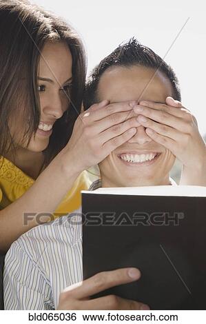 Stock Photograph - Girlfriend covering boyfriend’s eyes. Fotosearch