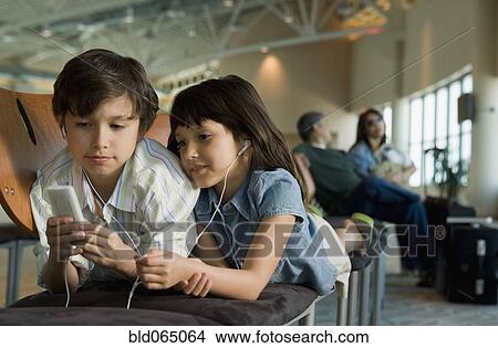 Hispanic brother and sister listening to mp3 player in airport View Large Photo Image Picture - Hispanic brother and sister listening to mp3 player in airport. Fotosearch