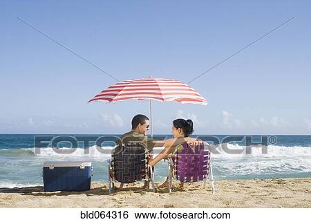 Stock Photograph - Hispanic couple relaxing at beach. Fotosearch