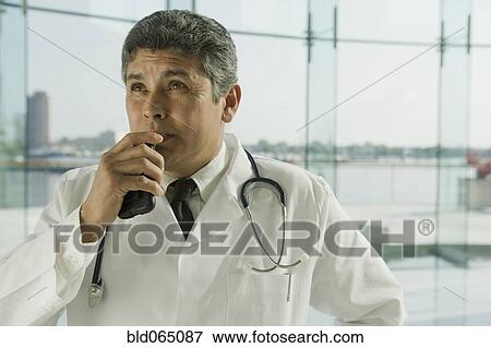 Stock Photo - Hispanic doctor in lab coat speaking into dictaphone. Fotosearch