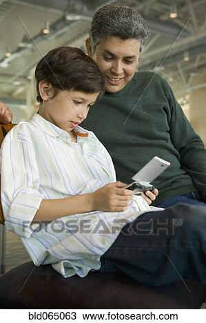 Stock Image - Hispanic father watching son play video game. Fotosearch