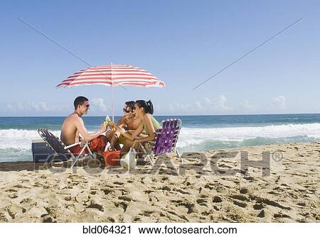 Stock Image - Hispanic friends relaxing at beach. Fotosearch