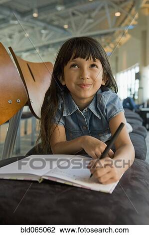 Stock Image - Hispanic girl writing in diary in airport. Fotosearch
