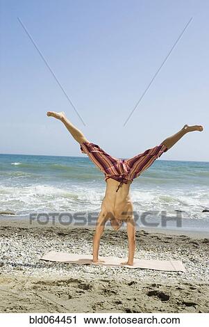 Stock Image - Hispanic man doing handstand on beach. Fotosearch