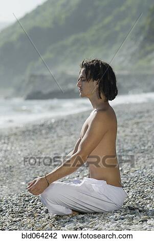 Stock Image - Hispanic man doing yoga at beach. Fotosearch