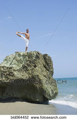 Stock Image - Hispanic man doing yoga at beach. Fotosearch