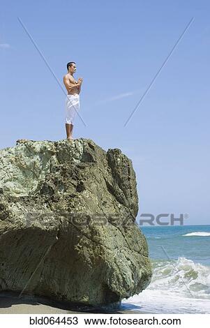 Stock Image - Hispanic man doing yoga at beach. Fotosearch