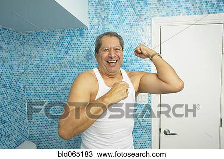 Stock Image - Hispanic man flexing his biceps in bathroom. Fotosearch