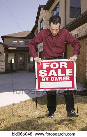 Stock Photo - Hispanic man placing for sale sign in yard. Fotosearch