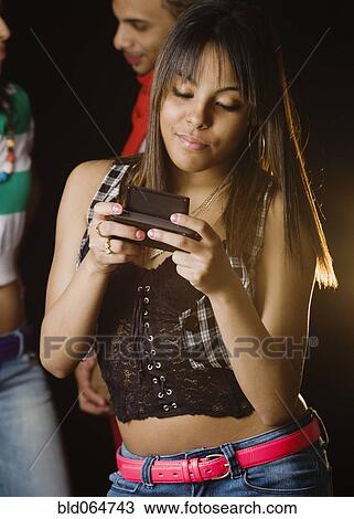 Stock Image - Hispanic teenage girl checking text messages on cell phone. Fotosearch