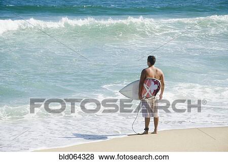Stock Photo - Hispanic teenager at beach with surfboard. Fotosearch