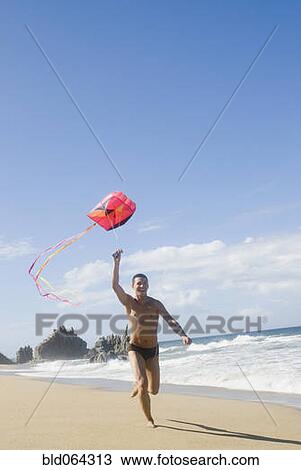 Stock Image - Hispanic teenager flying kite at beach. Fotosearch